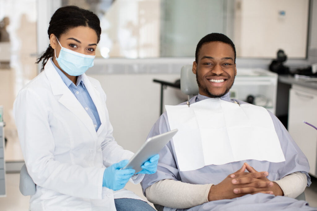 A dentist is having a quick dental-related interview with her patient while the patient is sitting on a dental chair.