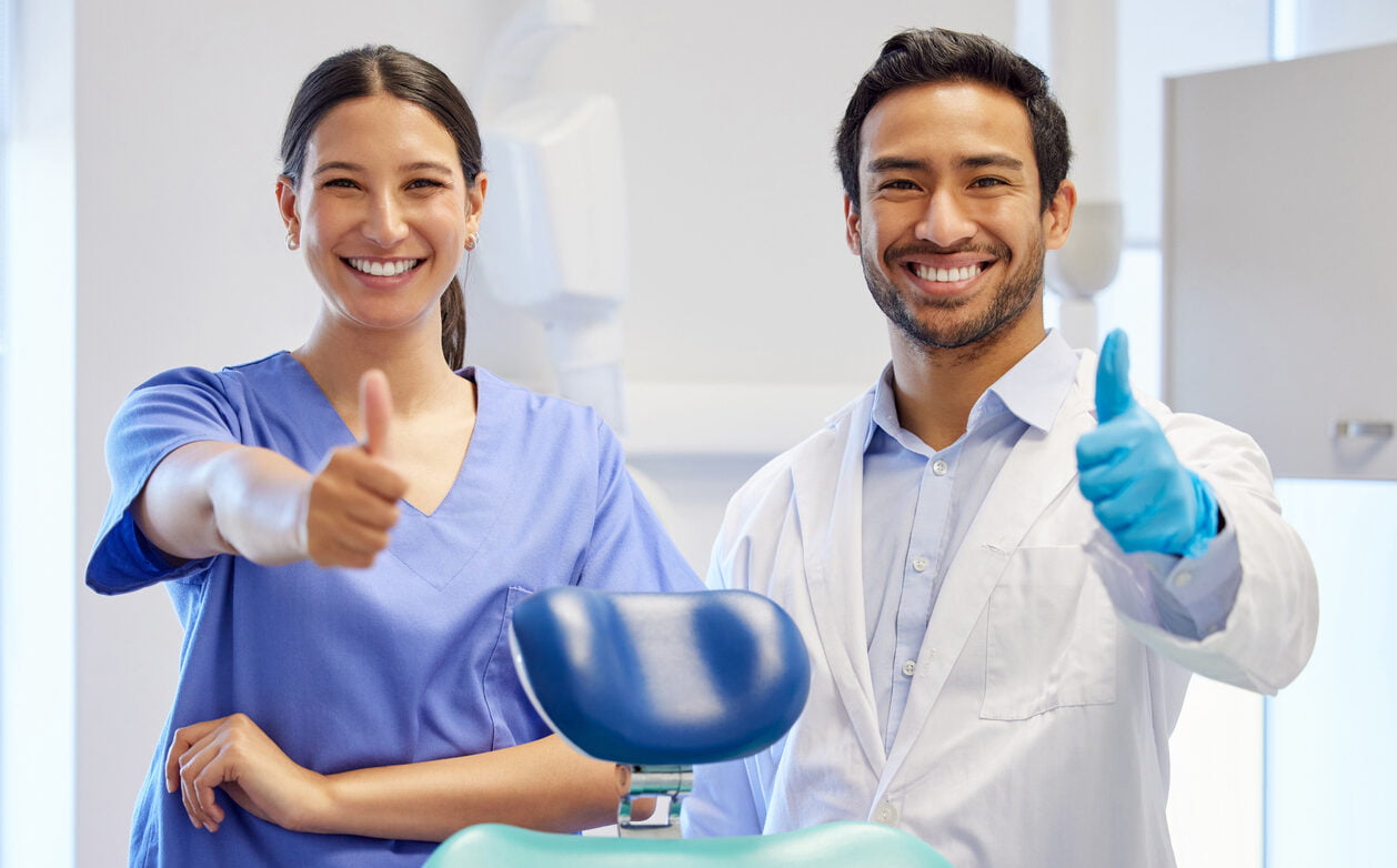 Portrait of two young dentists showing thumbs up in their consulting room.