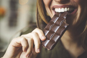 Close-up shot of a woman’s mouth biting a bar of chocolate.