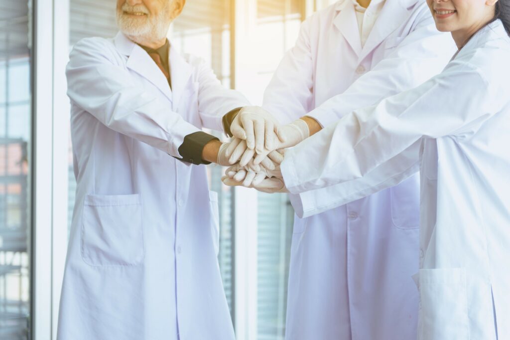 A group of professional healthcare providers coordinating hands in the laboratory.